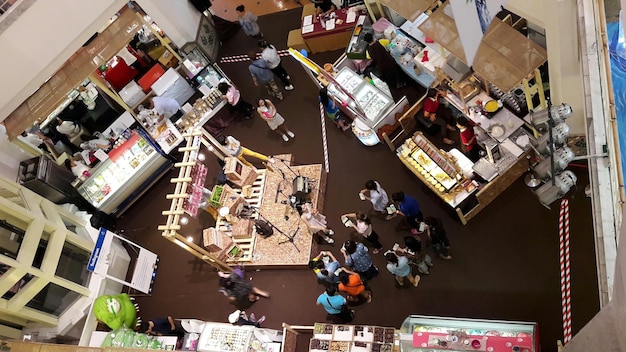 Wide aerial image showcasing a diverse and bustling grocery store aisle fully stocked with various Korean food products. Shelves are filled with recognizable brands of kimchi, gochujang, ramyeon, soy sauce, and other Korean sauces. Many shoppers examine the products.