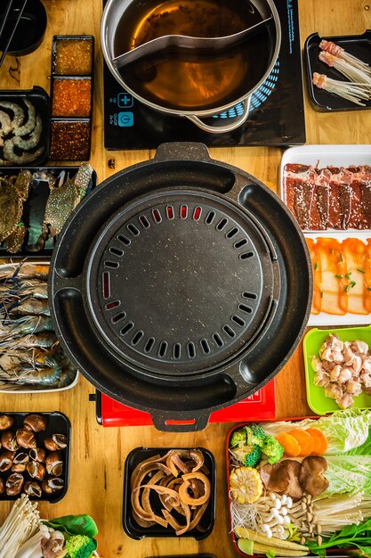 A close-up shot of a Korean BBQ grill with various meats cooking and an array of colorful banchan (side dishes) surrounding it. Focus on the sizzling meats and the variety of textures and colors of the banchan.