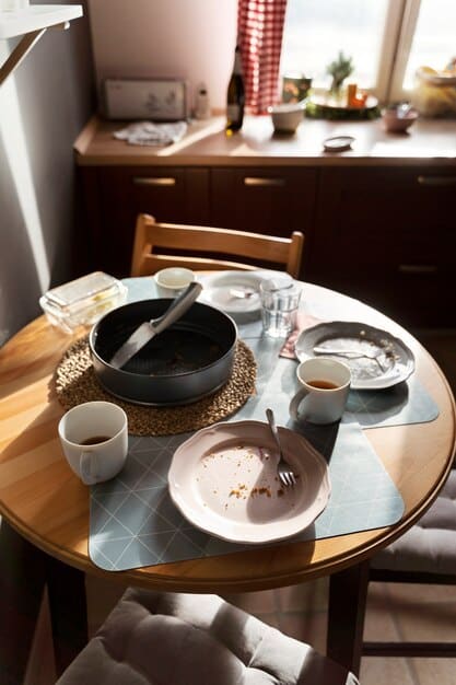 A detail shot of a Korean-style dining table with low seating cushions, simple ceramic dishes, and chopsticks. A window with sheer curtains provides soft lighting.