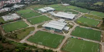 Vista aérea de um moderno centro de treinamento de futebol no Brasil, com campos de gramado impecável e estruturas tecnológicas.